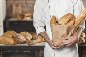 mid-section-male-baker-holding-paper-bag-with-breads